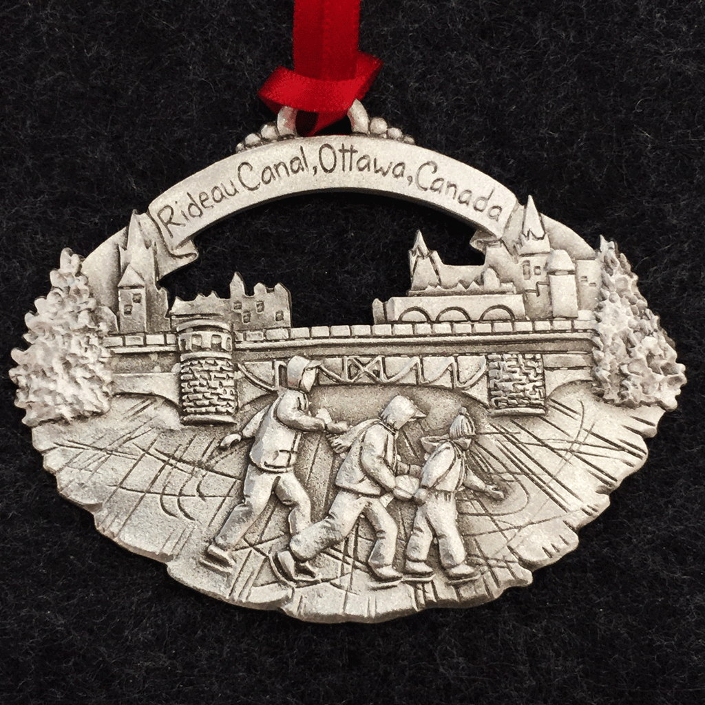 Three people skate on the Rideau Canal. The ice is scratched fromskates, and there is a bridge and buildings behind the three people. a pewter ribbon with Rideau Canal, Ottawa, Canada written in it arcs above the scene and attaches to a red ribbon. 