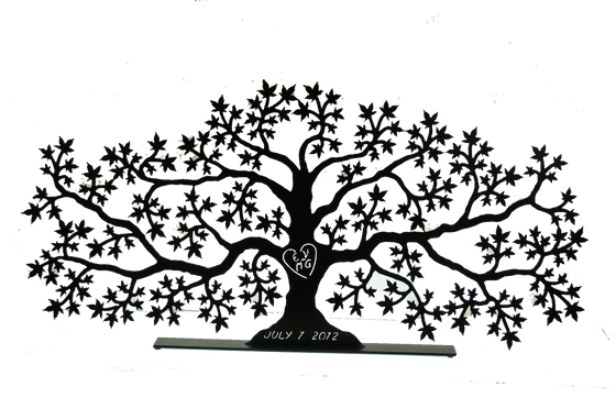 This metal sculpture shows the matte black silhouette of a sprawling maple tree, twice as wide as it is tall. Half way up the tree’s trunk the initials “EV + MG” have been carved through the metal, allowing light to pass though the sculpture. The initials are enclosed by a heart. At the base of the trunk is carved “July 1, 2012”. The piece sits on a narrow, rectangular base.